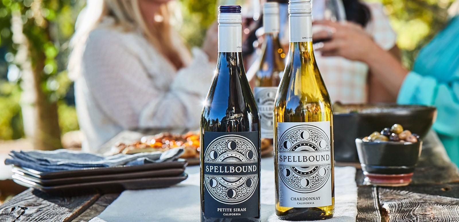 Two bottles of Spellbound wine with people having fun in background
